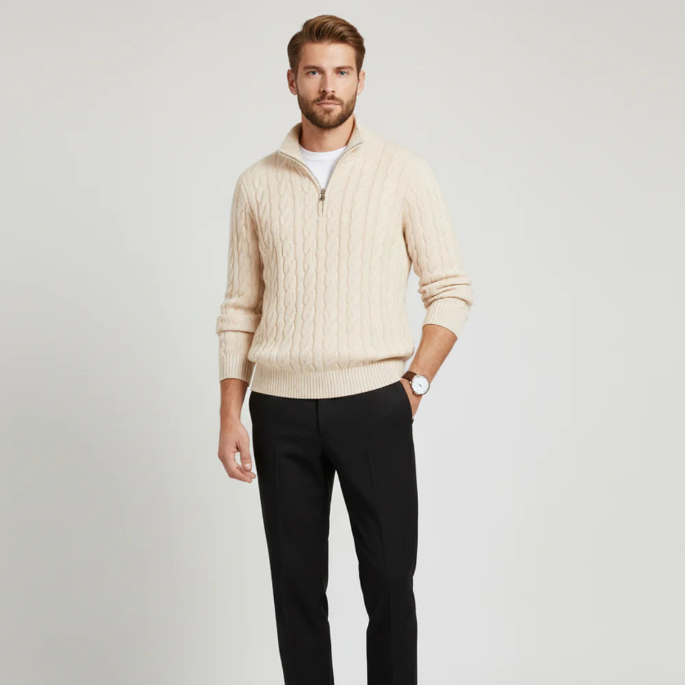 Man wearing a beige cable knit sweater and black pants on a light gray background