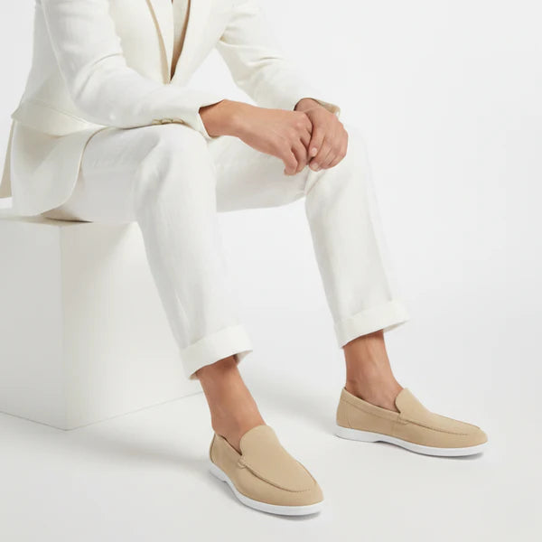 Person wearing a white suit with beige loafers on a light gray background